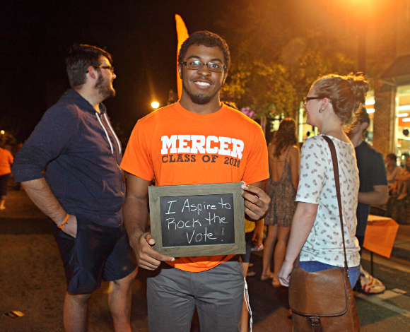 a student wearing a mercer shirt holds a chalkboard sign that says i aspire to rock the vote